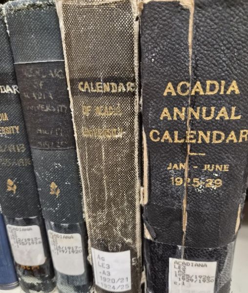 Four worn book spines of Acadia Calendars ranging from 1913 to 1929. The books are bound in dark coverings with partially faded gold lettering.